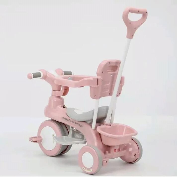 Pink children's tricycle with a handle on a white background